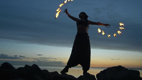 The girl makes a fire show against the backdrop of the sunset sky and the river