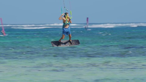 Young kiteboarder surfing in Mauritius jumps while riding around the turquoise lagoon. Kitesurfer splashes glassy ocean water while riding in Mauritius