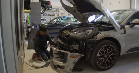Staten Island, New York United States - May 9, 2022: Auto repair technician removes front bumper from vehicle damaged in front end collision. Auto repair collision body shop interior.