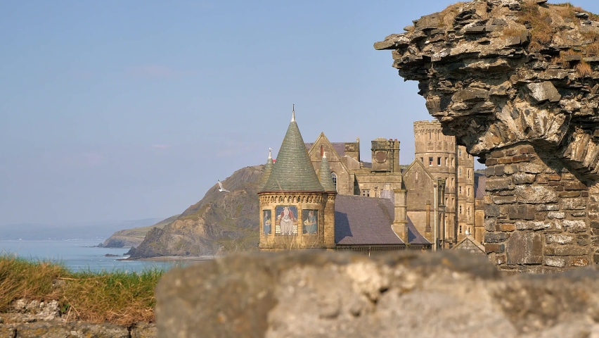 Aberystwyth, Ceredigion, West Wales. View of the spires of the Old College building and the coast beyond from behind a wall at Aberystwyth Castle on a sunny day and bright blue sky.