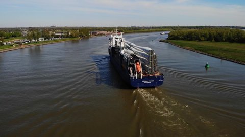 Barendrecht , Netherlands - 04 18 2022: Aerial Stern View Of Symphony Provider Cargo Ship Transporting Transporting Wind Turbine Propeller Blades Along Oude Maas. Dolly Back Rising