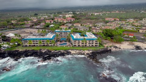 Kailua-Kona Town with ocean waves washing ashore near the Kona Reef Resort and other hotels at Kahului Bay on the Big Island of Hawaii - pull back ascending aerial