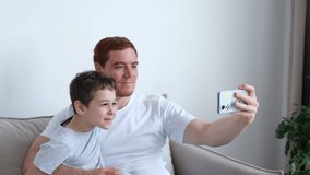 Happy father and little son sit relax on couch in living room have fun using cellphone together. dad and boy child rest on sofa at home watch funny video on smartphone