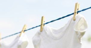 White baby clothes hanging on rope outdoors on spring day.