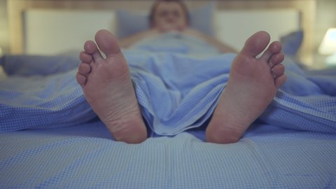 Bare feet of a man in close-up lying in bed in the evening before going to bed