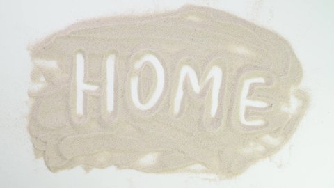 Home. Top view draw on the sand. Caucasian hands write text in beige sand. Vacation and travel. Beach on vacation. Sand painting. Creativity from natural materials.