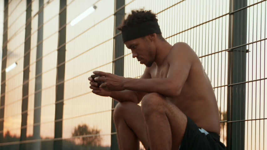 African American male sits on a ball and using his phone on basketball court. Shot with 2x anamorphic lens | Shutterstock HD Video #1090263307