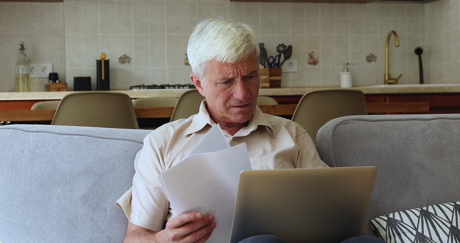 Stressed older male manage papers at home using laptop unable to pay bills deal with wrong work complicated interface of web bank app. Worried aged grandpa find loan debt reading financial documents Royalty-Free Stock Footage #1090263741