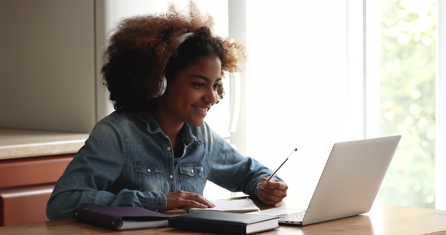 Busy African teen female high school pupil college student sit at table by laptop in headphones listen to video lesson at home write up information. Gen z lady prepare essay homework using modern tech Royalty-Free Stock Footage #1090263753