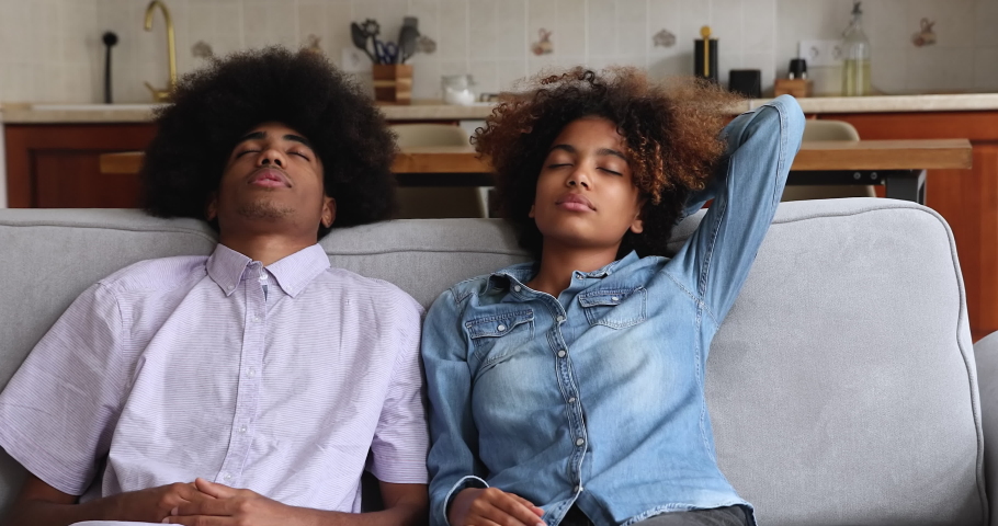Serene Black family couple rest on comfortable sofa at own rented purchased apartment sit in comfy poses keep eyes closed relax. Peaceful young husband wife enjoy lazy pastime breath clean fresh air Royalty-Free Stock Footage #1090263761