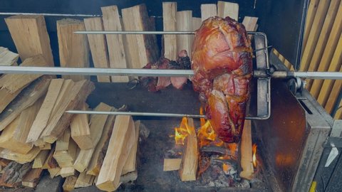 Delicious ham rotating in street grill. European street food. Big piece of pork cooking on a spit at street festival