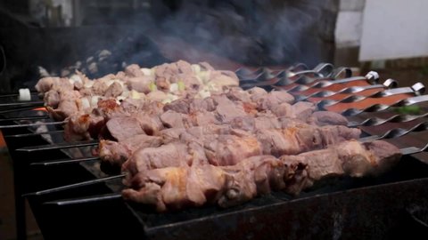 Preparing pork shashlik on a charcoal mangal. Beef grill. BBQ. Marinated meat food cooking on a mangal skewers on the fire. Top view. Outdoor picnic rest. Traditional tasty shish. Smoke. Juicy meal.