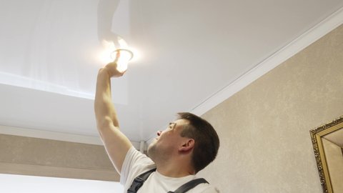 A male electrician changes the light bulbs in the spotlight ceiling lamp. men's household duties. care of electrical appliances at home.