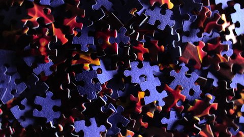 Background of Colored Puzzle Pieces that Rotating Counterclockwise - Top View. Texture of Incomplete Red and Blue Jigsaw Puzzle with Low Key Light - Left Rotation