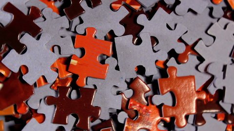 Background of Colored Puzzle Pieces that Slowly Rotating Counterclockwise - Top View, Close-Up. Texture of Incomplete Red and Grey Jigsaw Puzzle - Left Rotation