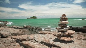 Stones balance on reef rock with a island on background of sea and blue sky on summer season at Thailand