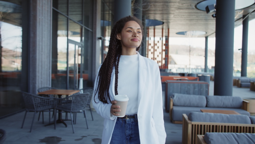 Beautiful woman walking speak on mobile phone hold paper cup. Smiling, talking on phone. Relaxing outdoors on street. Slow motion