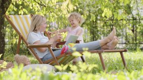Happy smiling family in green garden, sunny summer day. Mother and her little child girl have fun together playing and drinking orange juice. Mom on break from using laptop spends time with daughter - Powered by Shutterstock - Get 15% off with code: PIKWIZARD15