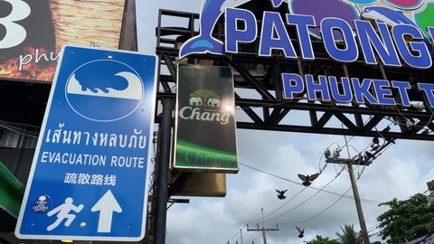 Phuket, Thailand - May 15, 2022: Tsunami evacuation route sign is seen in Bangla road, Patong beach, southern Thailand. The sign is written in Thai, English and Chinese language.
