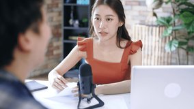 Cheerful young Asian female podcaster holding a questionnaire while interviewing guest at workspace with mic and laptop - Powered by Shutterstock - Get 15% off with code: PIKWIZARD15