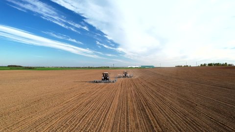 Tractor sowing seed on plowed field. Sowing seeds of corn and sunflower. Blue Tractor with disk harrow on plowing field. Seeding machinery on farm field. Seed sowing in farmland, aerial view.