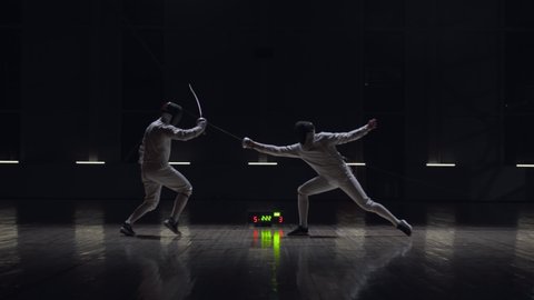 Two professional male fencers having a sabre fight in against dark background