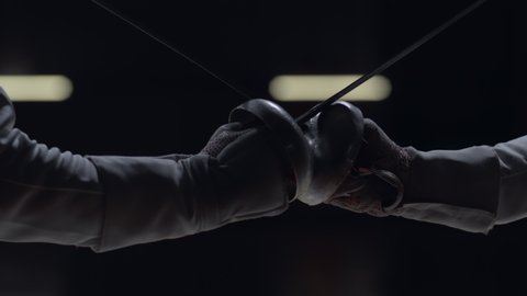 CU Two professional male fencers having a sabre fight in against dark background