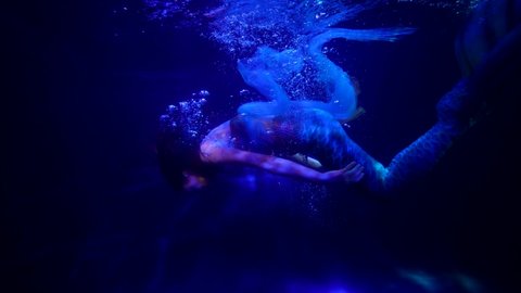 the mermaid swims with pleasure in the blue water with bubbles. the streaks of red light are sliding. the general plan