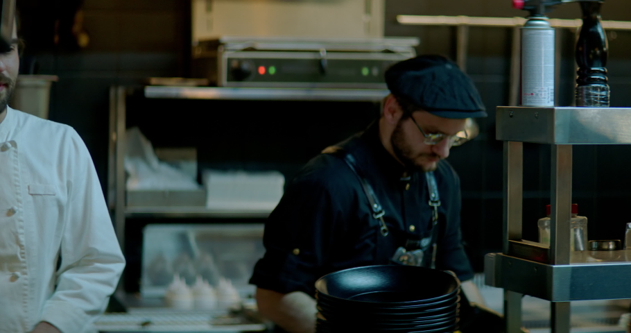 TRACKING Positive chef walking through busy commercial restaurant kitchen, talking and cheering kitchen crew. Shot with 2x anamorphic lens Royalty-Free Stock Footage #1090283135