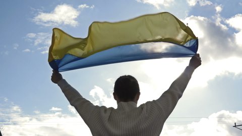 Woman holds a waving flag of Ukraine against a blue sky.
