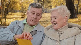 Smiling elderly couple aged partners grandparents senior wife husband open incoming postal envelope reads good news mail letter bank loan paper married pair sits on bench in park celebrating success - Powered by Shutterstock - Get 15% off with code: PIKWIZARD15