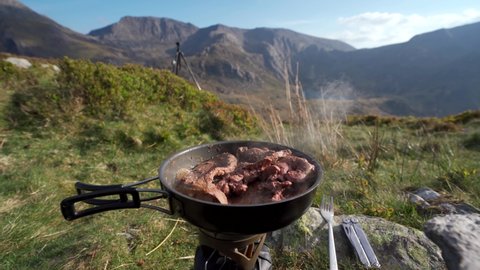 Steak and liver frying in a pan while camping in the mountains of Wales with a view of Tryfan: film stockowy