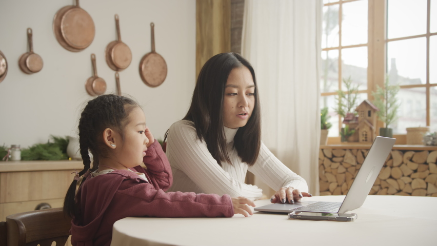 Mother teaching her daughter a lesson on her laptop indoors | Shutterstock HD Video #1090283723