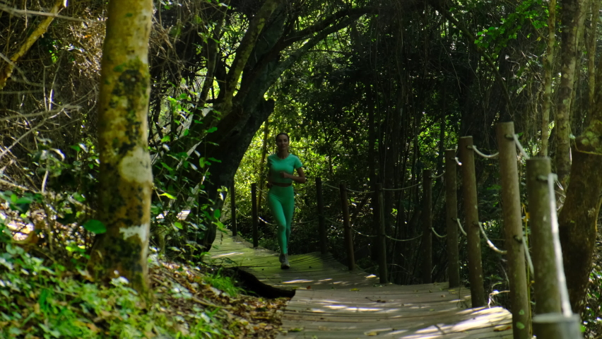Pretty sporty woman jogging at park in sunrise light. Beautiful young sporty american woman running at early morning jogging with jungle sunrise scene in background. Active healthy lifestyle. Running