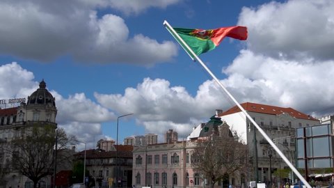 Coimbra, Portugal - May 01 2022: Waving Portuguese National Flag of Portugal with European Architecture Buildings in Background and blue sky