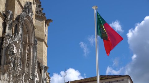 Coimbra, Portugal - May 01 2022: National Flag of Portugal Europe waving with Blue Sky and Santa Cruz Cathedral in background