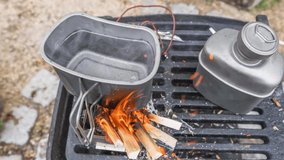 Footage of burning stainless steel hobo stove with titanium mug being boiled water on a barbecue outdoors, Germany