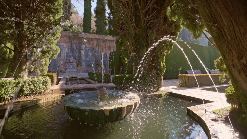 Slow motion gimbal shot of fountain surrounded by trees in Gardens of the Generalife in Alhambra. Granada, Spain.