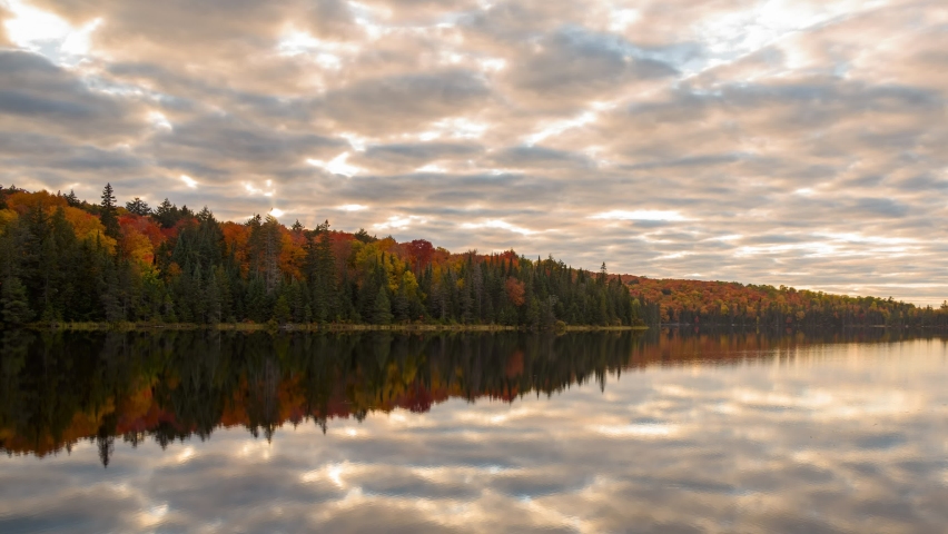 Moving clouds over a lake surrounded by dense forest at the peak of autumn colours at sunset - time lapse - Algonquin Provincia Park, ON, Canada