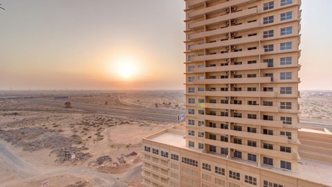 Sunset in Ajman aerial view from rooftop timelapse. Evening view of sun on orange cloudy sky behind a recidential tower in the United Arab Emirates.