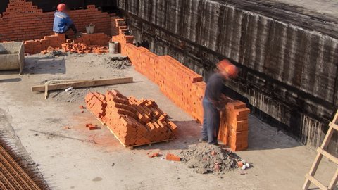 Bricklayers laying bricks to make a walls timelapse. Construction site of a new metro station. Professional workers in uniform adjusting bricks