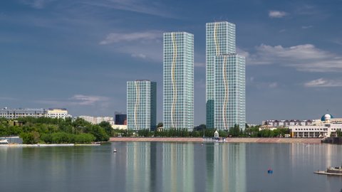 Yesil river timelapse with modern towers of residential complex in Astana. Park and waterfront on the side. Nur-Sultan city, Kazakhstan