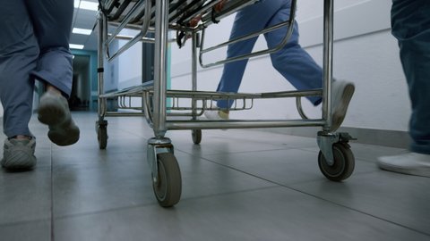 Doctors feet running down hospital corridor with gurney close up. Unknown medics team moving quickly to emergency room. Medical professionals pushing stretcher hurrying on operation. Health concept.: film stockowy