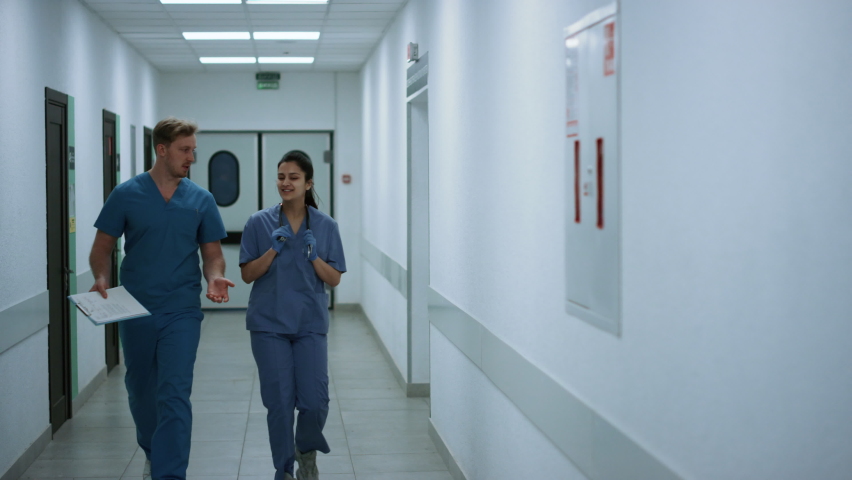 Two doctors walking down hospital corridor discussing patient diagnose. Young physician consulting woman colleague going emergency room. Couple professional surgeons talking hurrying to operation. Royalty-Free Stock Footage #1090290993