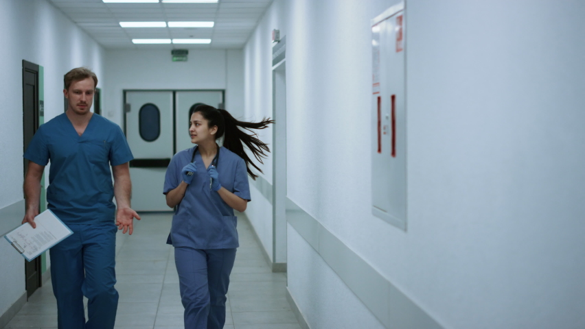 Two doctors walking down hospital corridor discussing patient diagnose. Young physician consulting woman colleague going emergency room. Couple professional surgeons talking hurrying to operation. | Shutterstock HD Video #1090290993