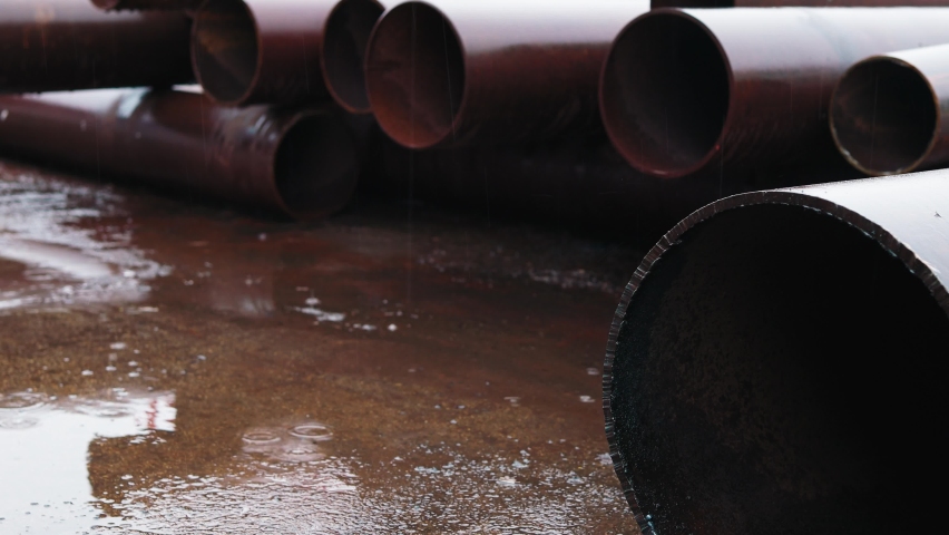 Metal pipes for gasification of large diameter lie on construction site in rain. Video. Pipes lie in puddle and it is raining. Concept of stopping construction of gas pipeline. Royalty-Free Stock Footage #1090292059
