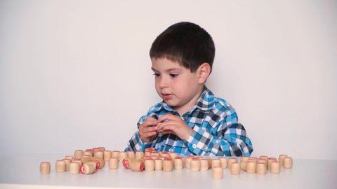 A preschool boy plays lotto, folds barrels with numbers on the table. The child learns to count