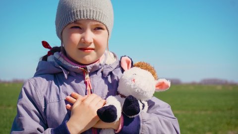 Serious little girl in field. Kid with toy plush cow looks into camera. Daughter with soft friend in spring day. Concept of peaceful and carefree childhood