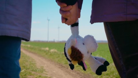 Close up plush cow toy in hand of ukrainian girl refugee who walks with family to border by country road. Concept of peaceful and carefree life without armed conflicts