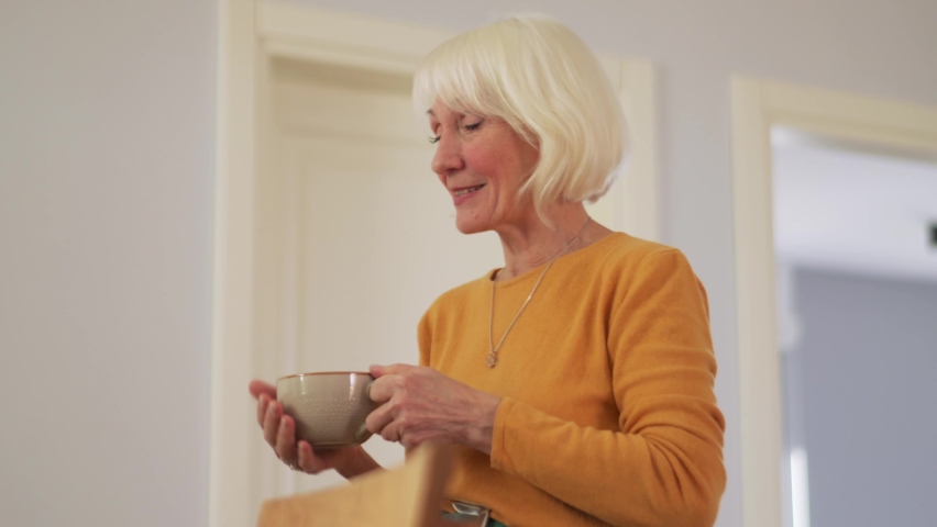 Handsome mature woman talking with a cup in the kitchen